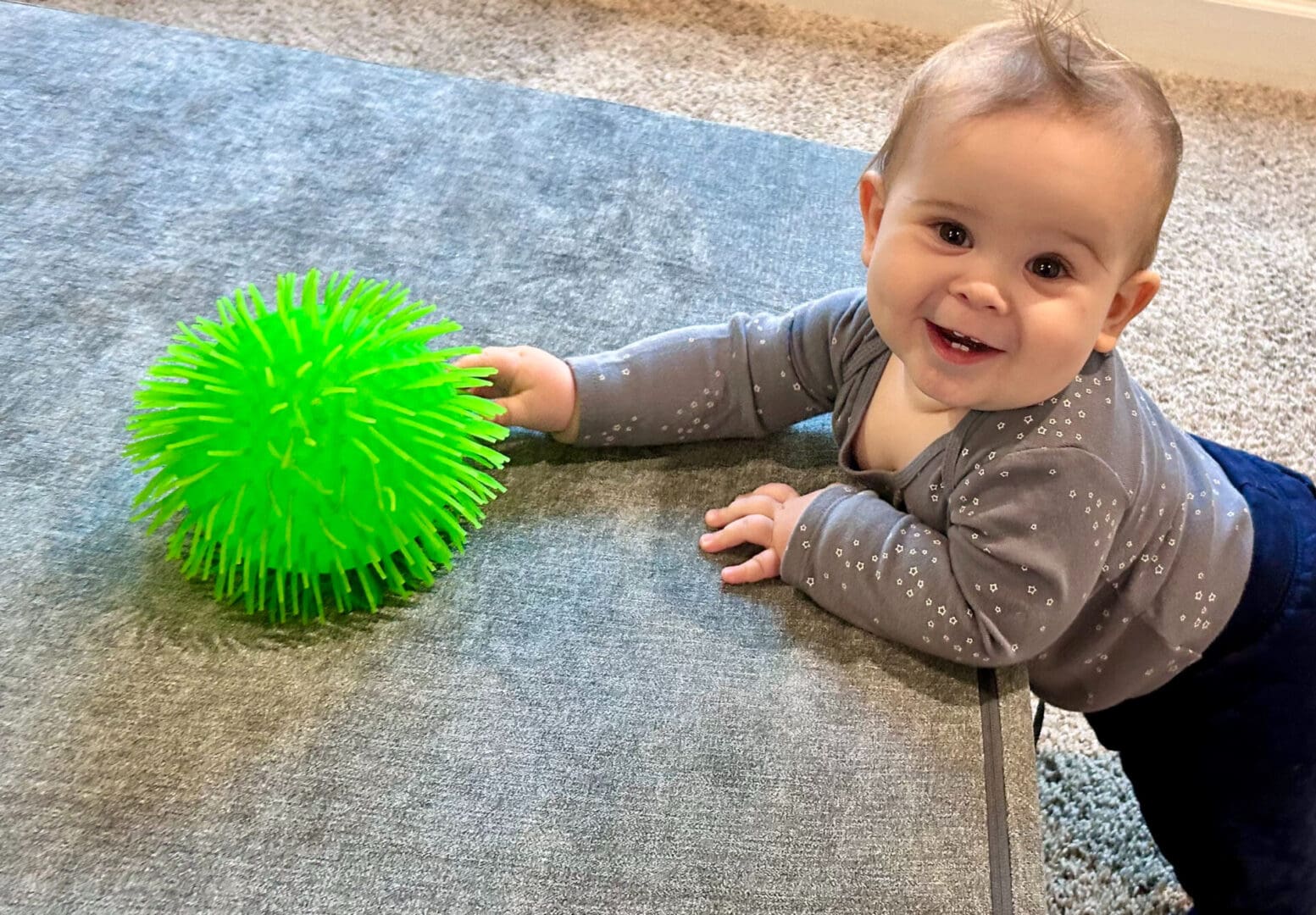 A baby is playing with a green ball.
